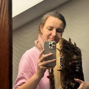 May include: A large, brown, faux-fur covered book with a spine of white teeth and decorative metal accents. The book has a weathered appearance and is held in front of a mirror.