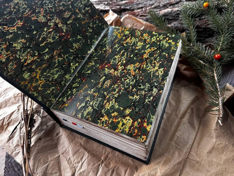 May include: An open book with a marbled green, yellow, and red cover. The book is lying open on a brown paper surface.