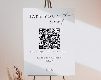 May include: White sign with black text that reads "TAKE YOUR seat" with a black and white QR code below. The text "Scan the QR code to find your seat" is below the QR code. The text "KATIE & MATTHEW 5.4.2X" is below that. The initials "KM" are at the bottom of the sign.