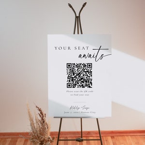以下が含まれることがあります： イーゼルに置かれた、黒文字とQRコードが書かれた白い看板。看板には「YOUR SEAT awaits」と「Please scan the QR code to find your seat」と書かれている。QRコードの下には「Medalya + Sanger」と「June 7, 202x | Kansas City」の文字がある。