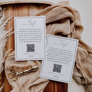 May include: Two white cards with black text that reads "a note on Gifts" and a message about wedding gifts. A gold wax seal and three gold wax seals are on a wooden surface with a beige cloth.