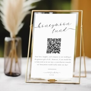 Può includere: Un cartello bianco con testo nero e un codice QR in una cornice dorata. Il cartello recita "honeymoon fund" e include un messaggio che chiede agli ospiti di contribuire alla luna di miele della coppia. Il testo include anche il nome "violet fnicholas" e il numero "6.7.2x".
