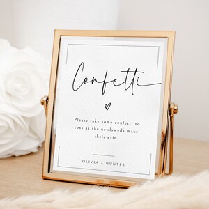 Könnte beinhalten: Ein goldfarbener Rahmen mit dem Wort "Confetti" in Kursivschrift. Das Schild enthält auch den Text "Bitte nehmen Sie Konfetti, um es zu werfen, wenn das Brautpaar seinen Abschied nimmt" und die Namen "Olivia + Hunter".