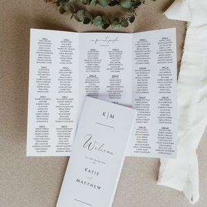 May include: A white wedding seating chart with the names of guests listed by table number. The chart is folded in thirds and features the text "our favourite people" and "Welcome to the wedding of Katie and Matthew" in black calligraphy. The date "May 4, 202X" and location "San Diego, California" are also printed on the chart.