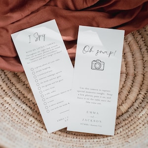May include: Two white cards with black text and illustrations. The left card has a checklist with the title "I Spy" and instructions to use a camera to find items at a wedding reception. The right card has a camera illustration and the text "Oh snap!" with instructions to use a camera to capture special moments at the wedding reception. The cards have the names "Emma J" and "Emma Jackson" and the date "6.7.202x" and location "Kansas City".