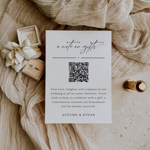 Könnte beinhalten: Eine weiße Karte mit schwarzem Text, der "a note on gifts" lautet. Unter dem Text befindet sich ein schwarz-weißer QR-Code. Der Text geht weiter: "Your love, laughter, and company at our wedding is all we need. However, if you wish to help us celebrate with a gift, a contribution towards our honeymoon will be warmly received. AUTUMN & ETHAN"