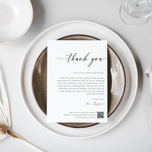 May include: A white thank you card with black calligraphy that reads "Thank You" and a message to family and friends. The card is on a brown plate with a white plate underneath. The card includes a QR code.