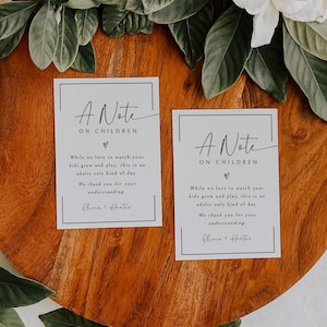 Puede incluir: Dos tarjetas blancas con texto negro que dice "A Note on Children" y un mensaje sobre un día solo para adultos. Las tarjetas están sobre una superficie de madera, con hojas verdes y flores blancas en el fondo.