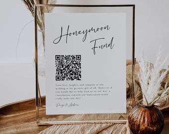 Puede incluir: Un cartel blanco con texto negro que dice "Honeymoon Fund" y un código QR. El cartel está en un marco dorado y está sentado en una mesa con un jarrón marrón y flores secas.