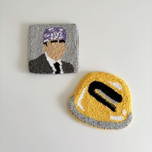 May include: Two handmade rug hookings, one depicting a man with a purple bandana and the other a yellow bell with a black handle.