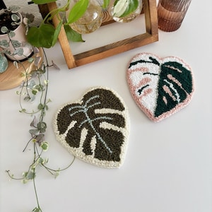 May include: Two handmade felt monstera leaf wall hangings. One is green and white, the other is pink, green and white.
