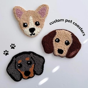 May include: Three custom pet coasters featuring dog faces. The coasters are made of yarn and feature a corgi, a dachshund, and a brown and white dog. The text "custom pet coasters" is written in black on a white background.