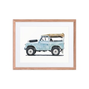 May include: A framed print of a light blue vintage SUV with a tan canvas roof. The vehicle has black tyres and a spare tyre on the bonnet. The artwork is set against a white background and framed in light brown wood.