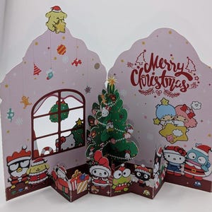 Peut inclure: Une carte de Noël pop-up avec divers personnages de dessins animés et un sapin de Noël décoré. La carte est rose avec les mots "Merry Christmas" en écriture rouge. La carte a une fenêtre avec une couronne et un personnage jaune portant un chapeau de Père Noël.