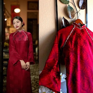 May include: A vibrant red, long-sleeved dress with a high collar and floral pattern. The dress features a decorative trim around the collar and is displayed on a wooden hanger. The image also shows a person wearing a similar dress.