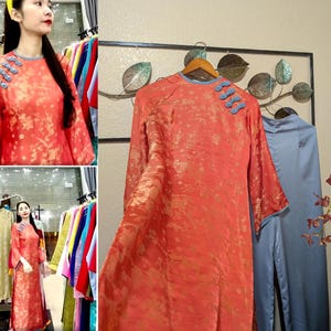 May include: A long, coral-colored dress with a floral pattern and blue trim. The dress has long sleeves and decorative blue buttons on the shoulder. A second blue dress is visible in the background.