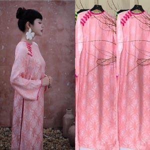 May include: A light pink, long-sleeved dress with a floral pattern. The dress has a mandarin collar and decorative buttons on the shoulder. The dress is shown on a person and also hanging on a rack.