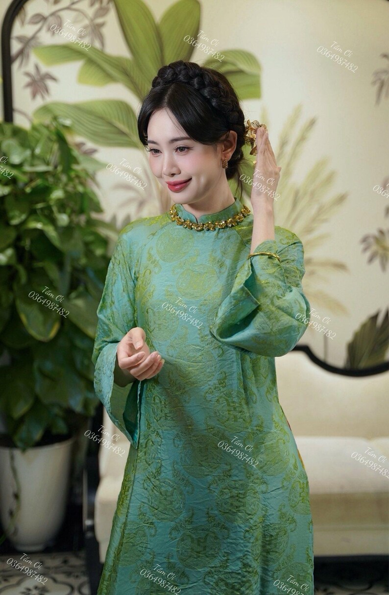 Op de afbeelding: Een teal en groen patroonjurk met lange mouwen en een mandarijnkraag. De jurk is versierd met een gouden ketting en armband. De afbeelding toont ook een vrouw met donker haar en een gouden haaraccessoire.