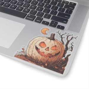 以下が含まれることがあります： ハロウィーンをテーマにしたステッカー。オレンジ色の目と口で笑うジャック・オ・ランタンが描かれています。三日月と木の枝が背景にあります。ステッカーはノートパソコンに貼られています。
