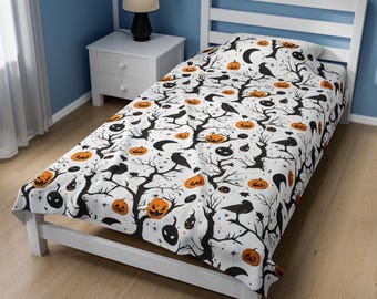Op de afbeelding: Witte eenpersoonsbedovertrek met een Halloween-patroon. Het ontwerp toont zwarte boomtakken, oranje pompoenen, zwarte kraaien en halve manen op een witte achtergrond. Het bed staat op een wit houten frame.