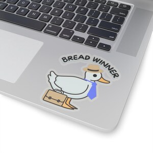 Op de afbeelding: Een sticker met een cartoon eend met een hoed, blauwe stropdas en een aktetas. De tekst "BREAD WINNER" staat erboven. De sticker is geplaatst op een laptop.