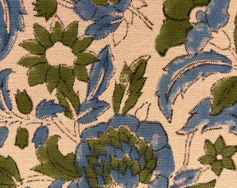May include: A woven fabric featuring a repeating floral pattern with blue and green petals and leaves on a cream-colored background. The design consists of stylized blossoms and foliage with visible texture and distinct outlines on the textile surface.