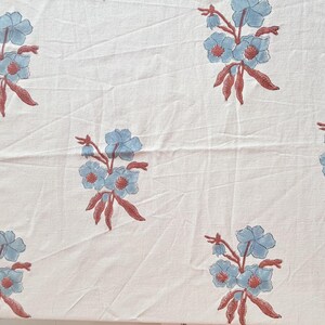 Könnte beinhalten: Weißer Stoff mit einem sich wiederholenden Blumenmuster. Das Design zeigt Gruppen hellblauer Blumen mit rotbraunen Stielen und Blättern. Die Blumen haben ein detailliertes, handgezeichnetes Aussehen und schaffen eine zarte und künstlerische Ästhetik.
