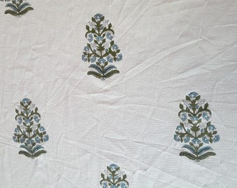 May include: White fabric with a repeating floral pattern. The design features stylized floral motifs in shades of blue, green, and gray. The fabric appears to be cotton or linen, with a slightly textured surface. The overall aesthetic is reminiscent of block printing.