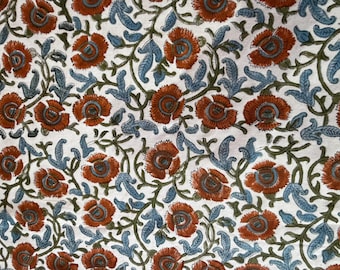 May include: Close-up of a fabric with a repeating floral pattern. The design features rust-colored flowers with blue-green leaves and stems on a white background. The pattern is detailed and symmetrical.