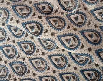 May include: Close-up of a fabric with a repeating paisley pattern. The design features teardrop-shaped motifs in shades of blue, gray, and brown against a cream-colored background. The fabric has a textured appearance, suggesting a woven material.