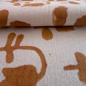 Puede incluir: Primer plano de una tela doblada con un patrón repetitivo. La tela es blanquecina con un patrón repetitivo de formas abstractas marrones. La textura de la tela es visible, lo que sugiere un material tejido.