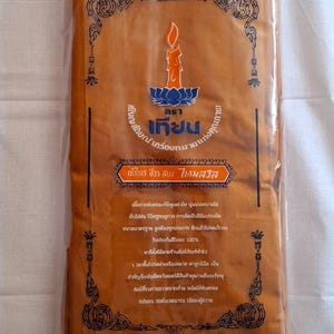 May include: A brown fabric package with a label that reads "Thara Teechon" and "Symbol of Quality". The label also includes a candle on a lotus flower and text in Thai.