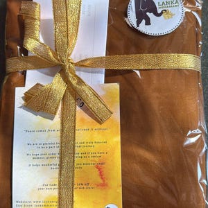 May include: A wrapped package in a clear plastic bag, tied with a gold ribbon and bow. The package is a warm brown color. A circular sticker with an elephant logo and text is visible. Includes a handwritten note.