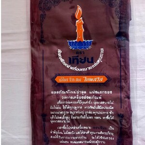 May include: A brown fabric package with a label that reads "ตรา เทียน" in Thai script. The label also includes a candle and lotus flower design. The text on the label describes the product as a "ไตร จีวร สบง ไหมสวัส" and includes information about the product's quality and size. The package is 200x300 cm.