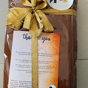 May include: A wrapped gift with a gold ribbon and bow. The gift is brown and has a tag that says "thank you." The tag also has text from the seller, Lanka Megamart, and a logo with an elephant.