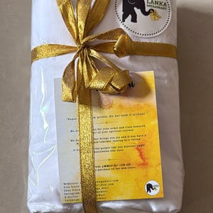 May include: A wrapped package tied with a gold ribbon and bow. A circular sticker with an elephant logo is visible. A small card with text is attached to the package. The package is white.