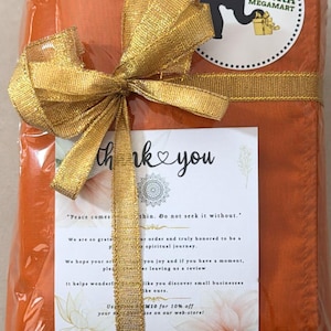 May include: An orange package wrapped in clear plastic and tied with a gold ribbon and bow. A white card with the words "thank you" and a logo is visible. The package has a sticker with an elephant logo and the words "Lanka Megamart".
