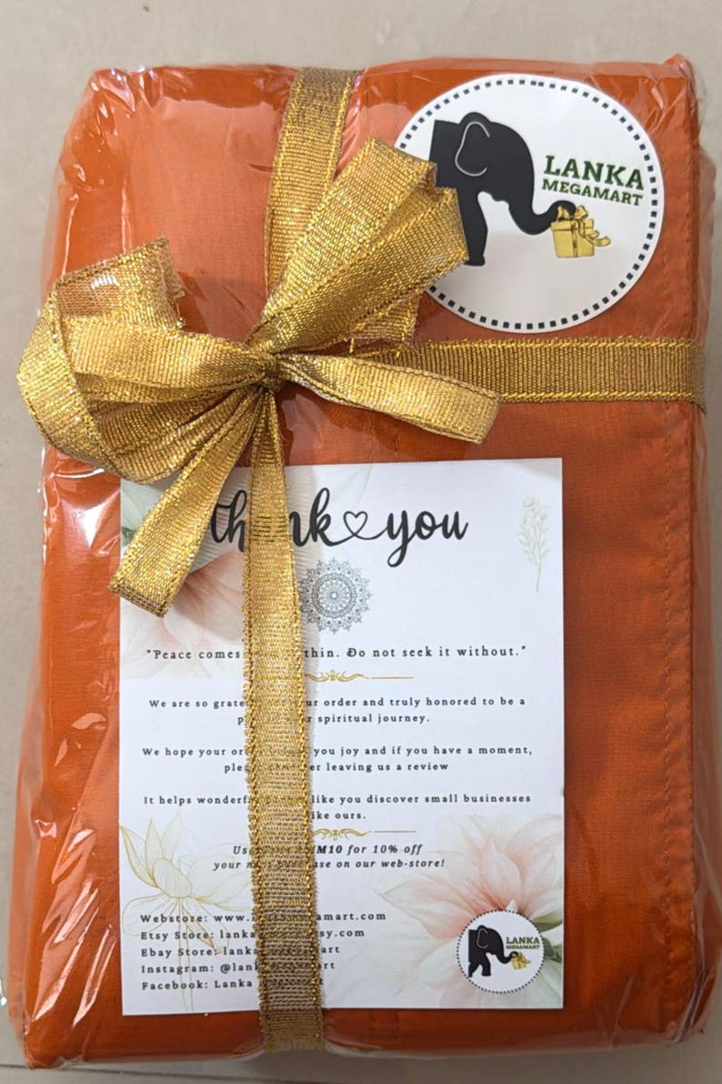 May include: An orange package wrapped in clear plastic and tied with a gold ribbon and bow. A white card with the words "thank you" and a logo is visible. The package has a sticker with an elephant logo and the words "Lanka Megamart".