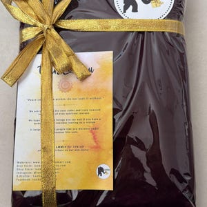 May include: A wrapped package in dark burgundy cellophane, tied with a gold ribbon and bow. A circular sticker with an elephant logo is visible. A small card with text is attached to the package.