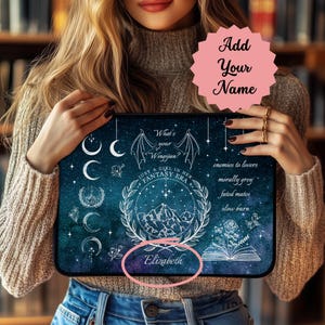 May include: A blue and black laptop sleeve with a white design featuring a crescent moon, stars, a mountain range, a book, and a bat with the text "What's your Wingspan?" and "Just a girl in her fantasy era." The text "Elizabeth" is also included in the design.