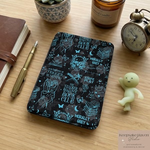 May include: Black phone case with a teal floral and skull pattern, featuring text like "The Stalker Romance Book Club" and "Morally Grey." The case also includes illustrations of books, butterflies, and a knife.