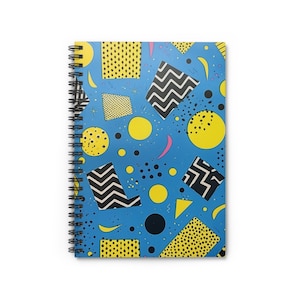 May include: A blue spiral notebook with a geometric pattern featuring yellow, black, and white shapes. The pattern includes circles, squares, and zigzags.