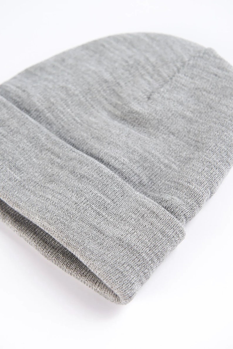 Puede incluir: Primer plano de un gorro gris. El gorro est&aacute; hecho de un material suave y tejido y tiene un borde doblado. El gorro es de color liso y neutro, adecuado para varios atuendos y estilos. El gorro tiene un dise&ntilde;o simple y cl&aacute;sico.