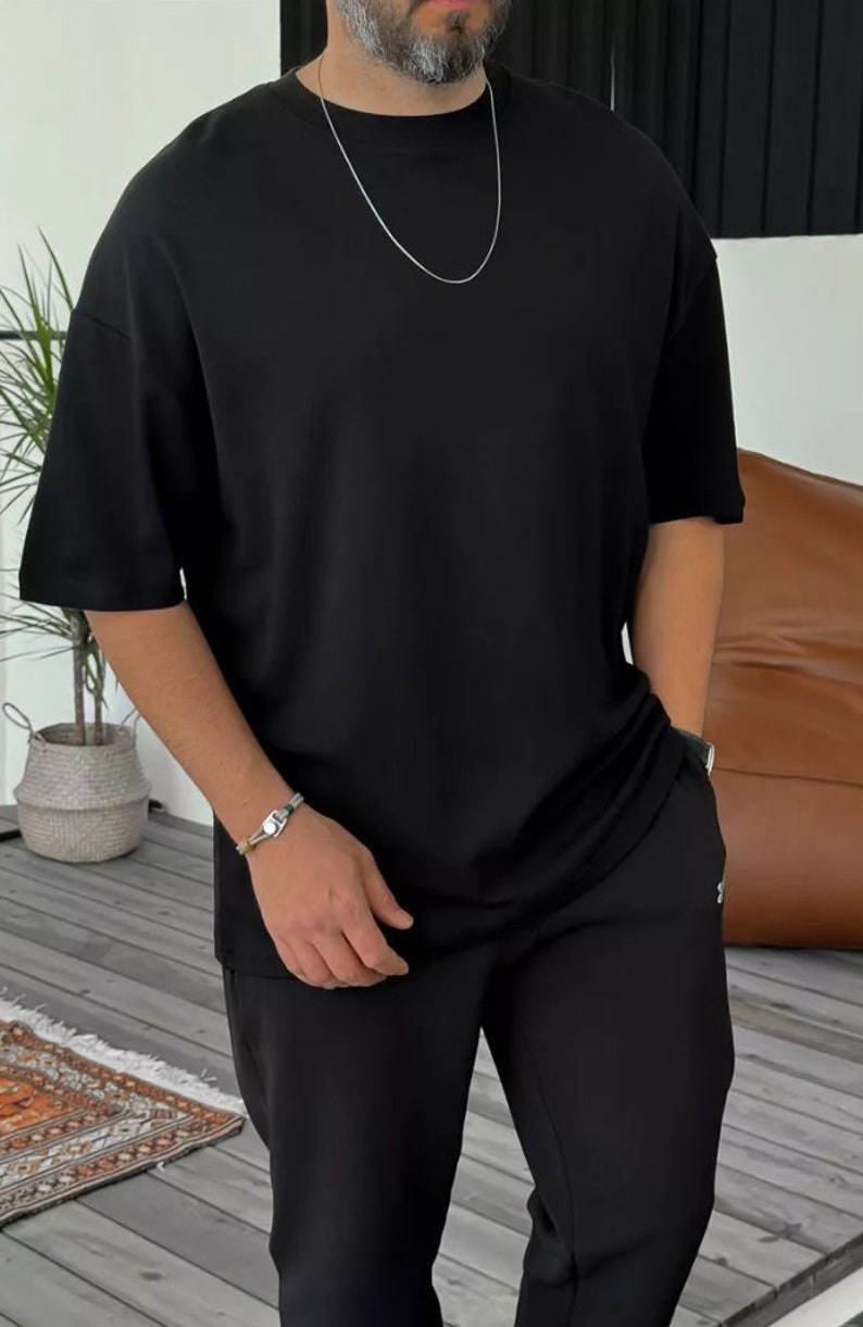 May include: A black oversized t-shirt with a silver chain necklace. The t-shirt is paired with black pants.