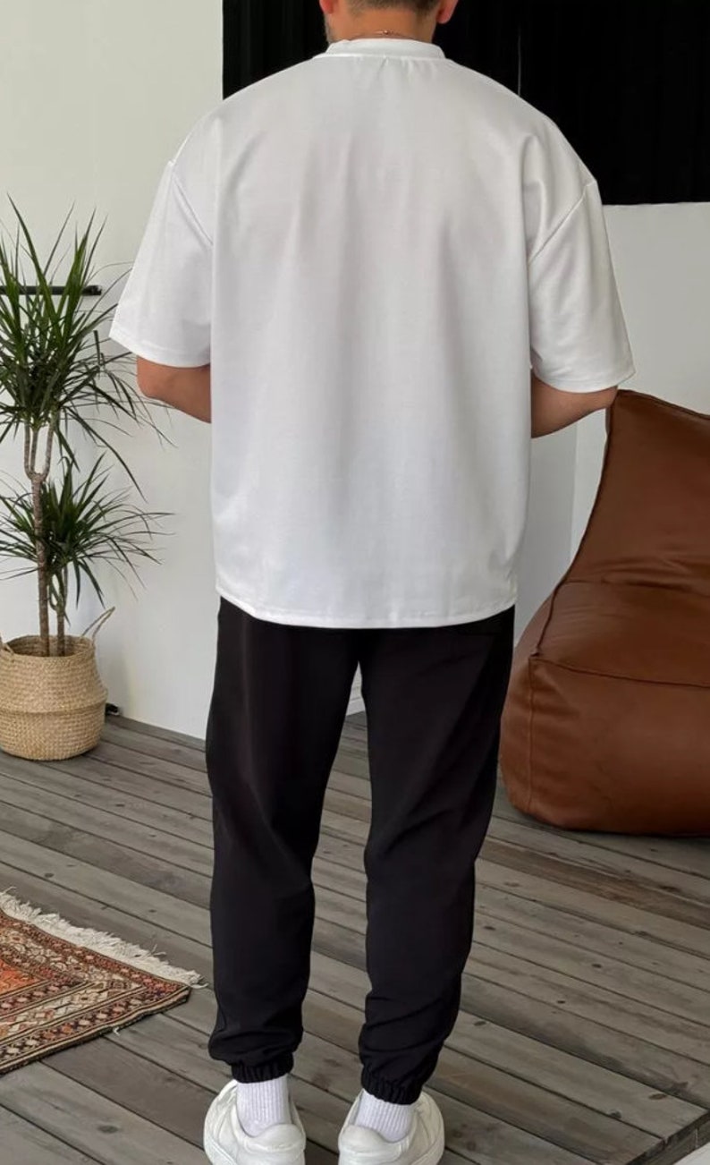 May include: A white short-sleeved t-shirt with a crew neck and black sweatpants. The person is wearing white sneakers.