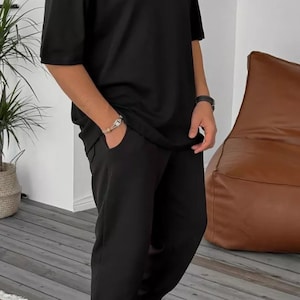 May include: A black short-sleeved t-shirt and matching sweatpants with a silver chain necklace and white sneakers.