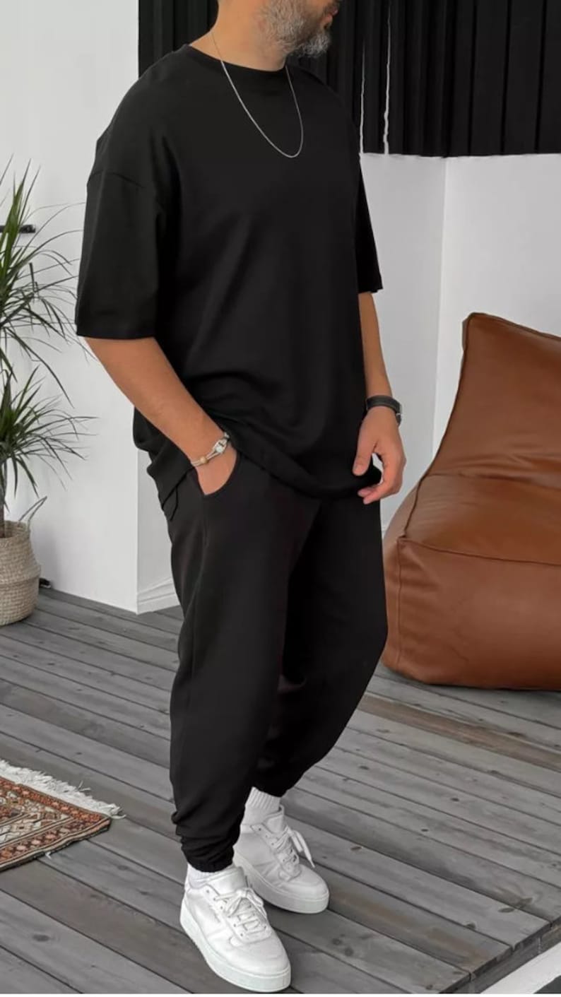 May include: A black short-sleeved t-shirt and matching sweatpants with a silver chain necklace and white sneakers.
