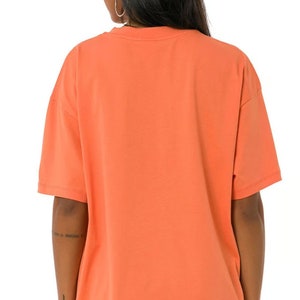 May include: A coral orange oversized t-shirt with short sleeves. The t-shirt is made of a soft, comfortable fabric.
