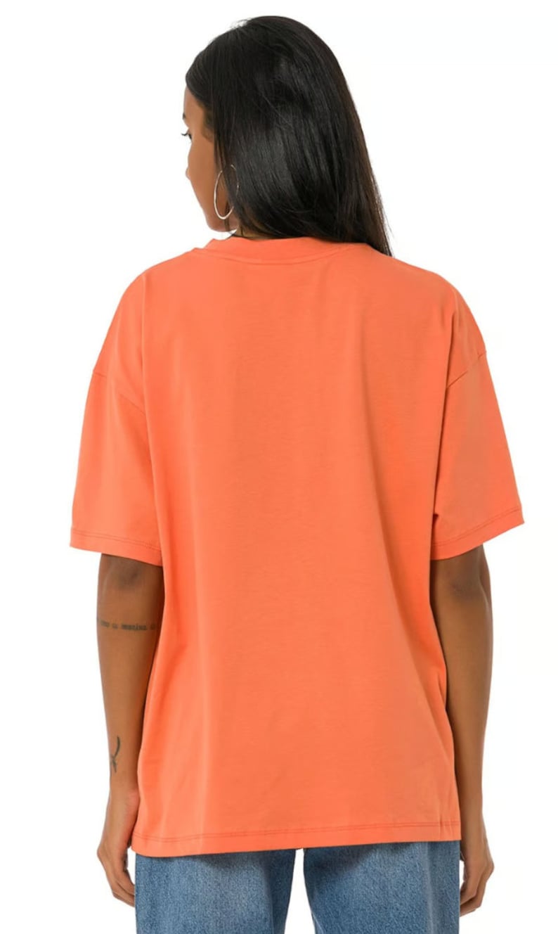 May include: A coral orange oversized t-shirt with short sleeves. The t-shirt is made of a soft, comfortable fabric.