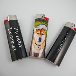 Pu&ograve; includere: Tre accendini rettangolari con cime metalliche e pulsanti di accensione rossi. L'accendino a sinistra &egrave; nero con il testo bianco PRODUCT EXAMPLES. Quello centrale mostra un cane con una corona di fiori. Quello a destra &egrave; nero con il testo bianco STICKER NOVA.